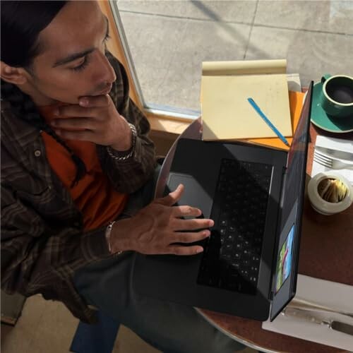 Person thinking while using a laptop at a cafe table.